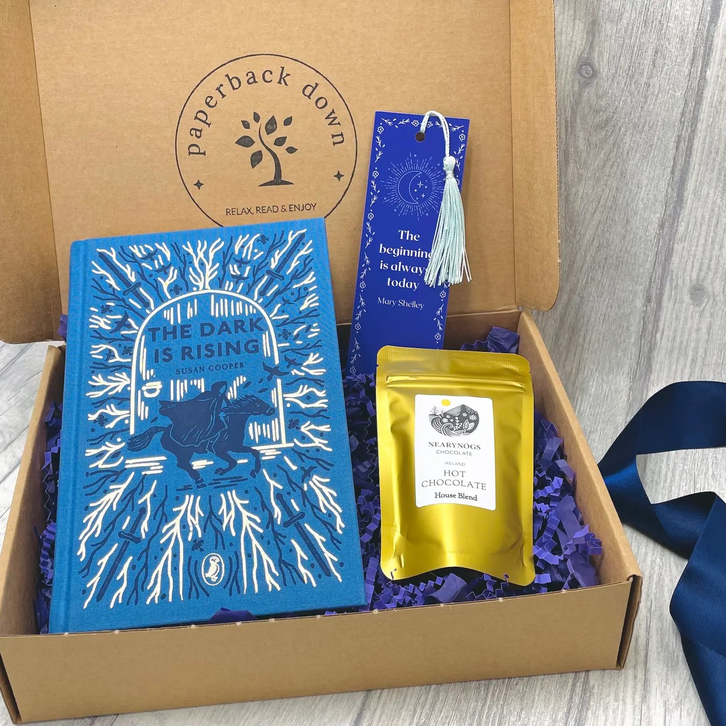 Book gift set with 'The Dark is Rising' book, hot chocolate and bookmark in a box labeled 'Paperback Down'.