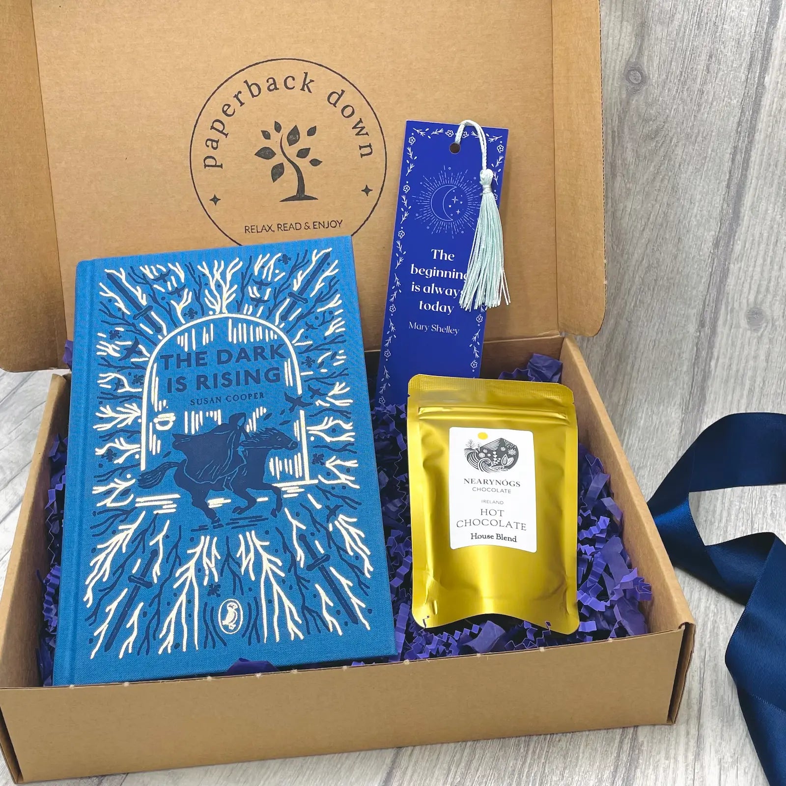 Book gift set with 'The Dark is Rising' book, hot chocolate and bookmark in a box labeled 'Paperback Down'.