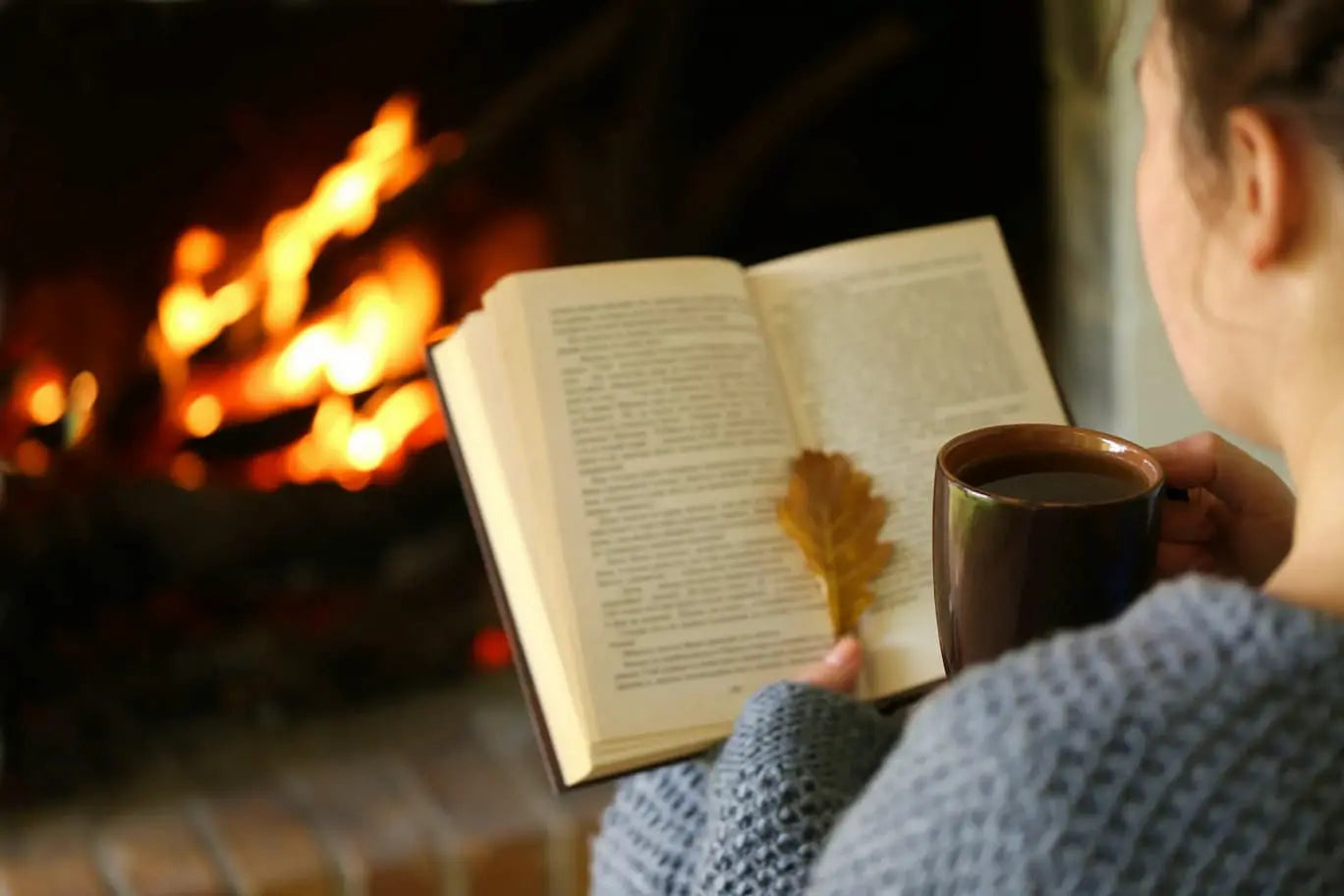 A picture of a woman enjoying a cosy autumn book in front of a fireplace