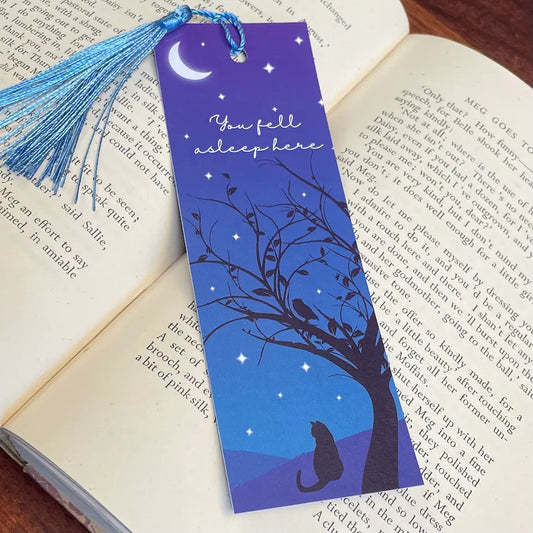 Bookmark featuring a black cat under the silhouette of a tree looking out across a starry sky, with the phrase 'you fell asleep here'.