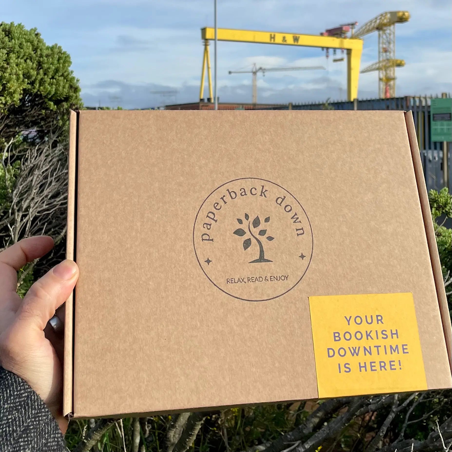 An image of a book subscription box for book-lovers, by County Down based small business Paperback Down, that features books by Irish and Northern Irish writers. In this image the gift box is displayed in front of a prominent Belfast landmark.