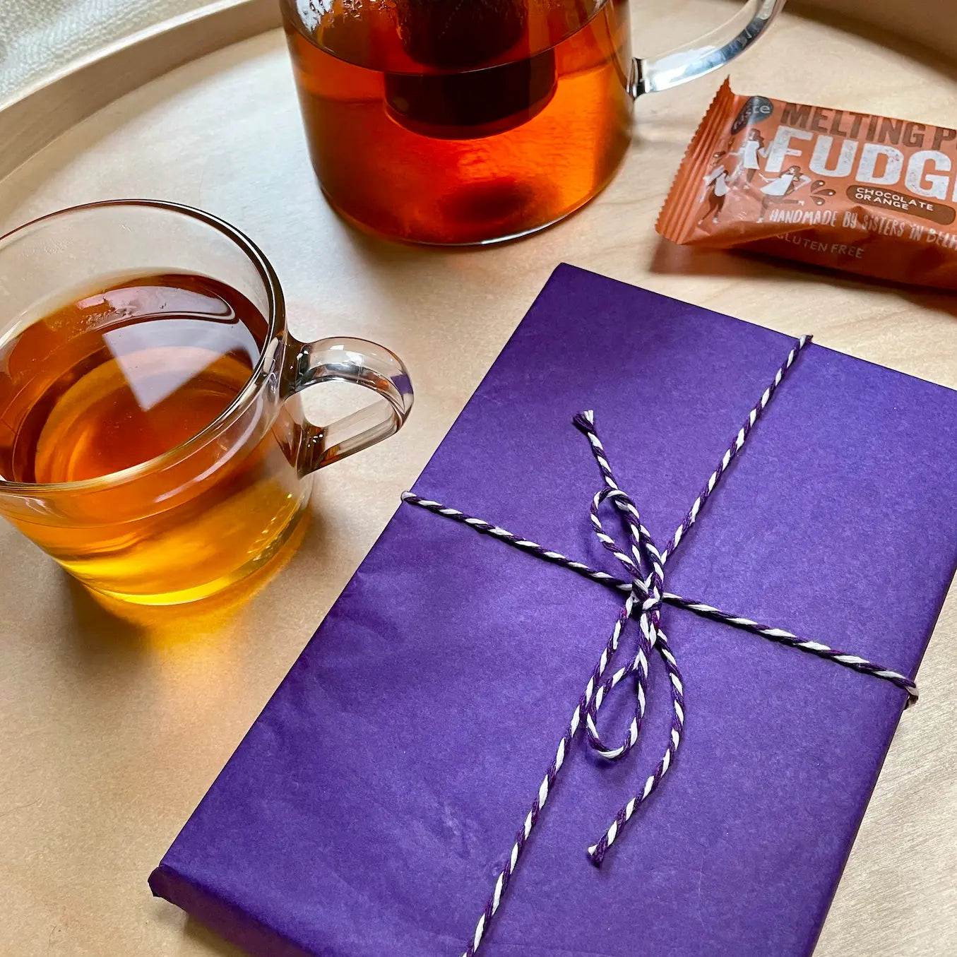 The image shown is of a beautifully wrapped new book, on a tray, beside which sits a chunky bar of Belfast-made fudge and a mug of tea.