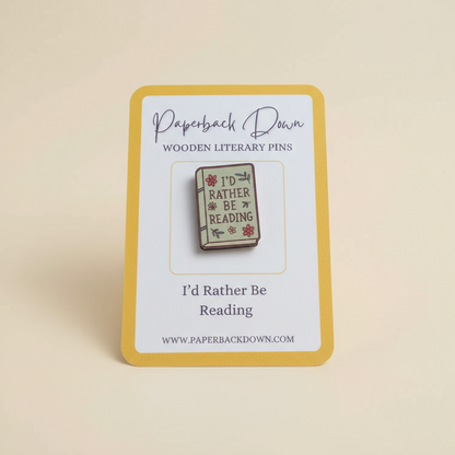 Wooden literary pin with 'I'd Rather Be Reading' text on a card, branded 'Paperback Down'.